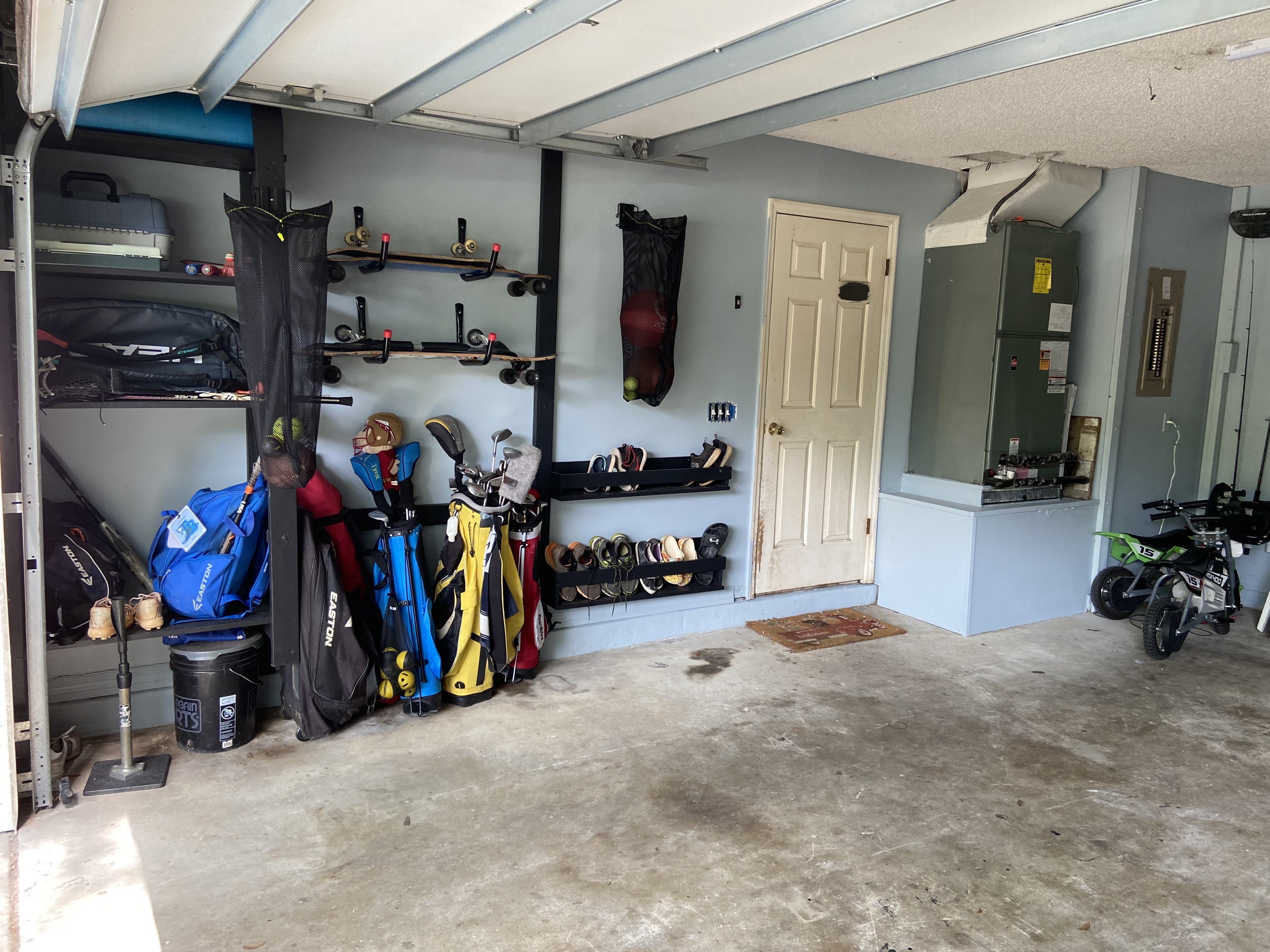 Garage after reorganization - 
		Painted in a calming blue,  I built the garage shelf system to provide ample storage for our various sports 
		equipment.  All shelving was stained to match the workbench on the opposite side. 
		Custom made shoe racks mounted off the ground.